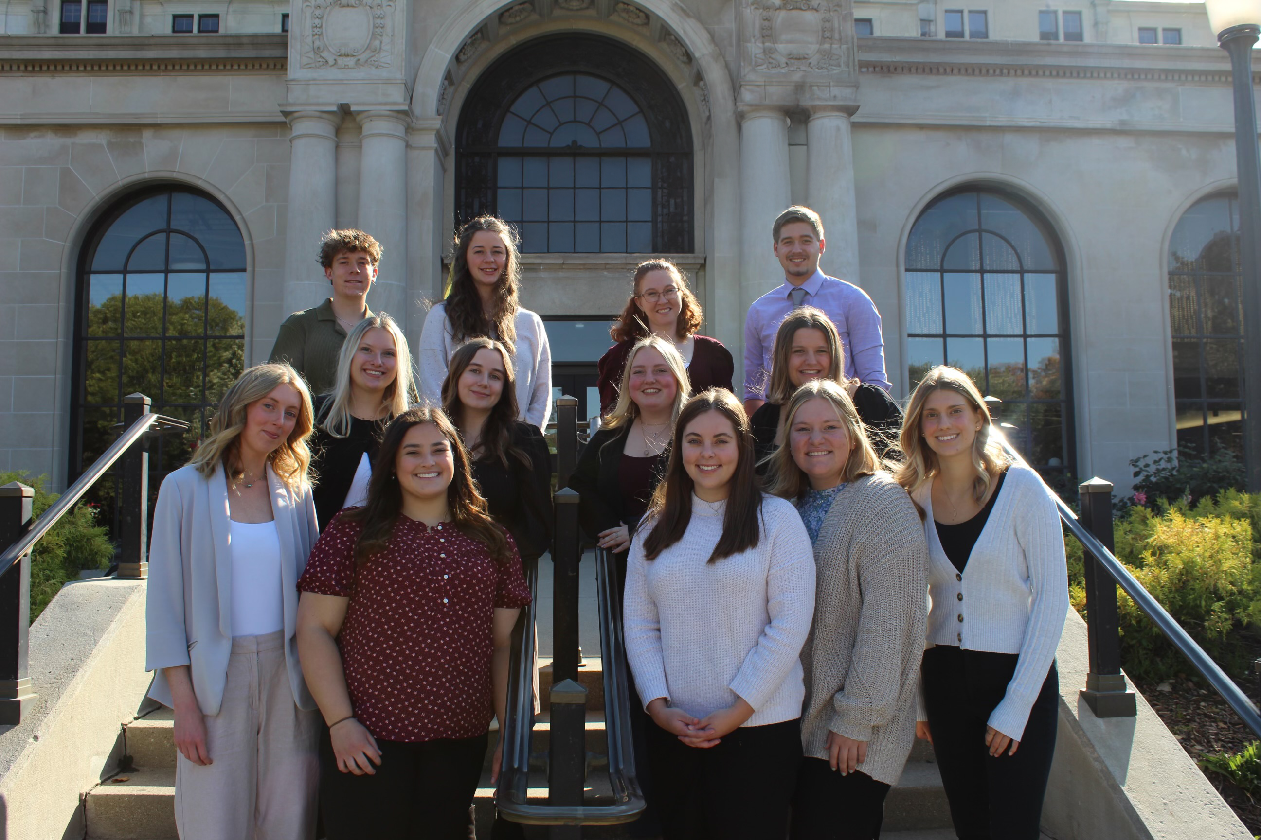 Group of 13 students standing on the steps of the memorial union on a sunny day after the induction ceremony.