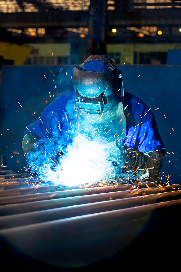 Worker dressed in protective uniform welding metal frame