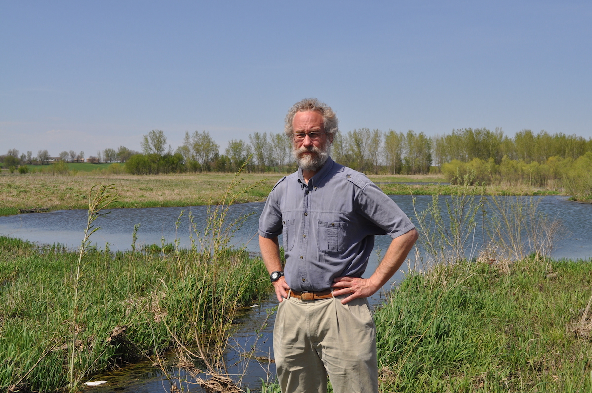 Dr. William Gutowski standing in the foreground. A small pond appears in the middle ground. Trees and houses in the distant backbround.