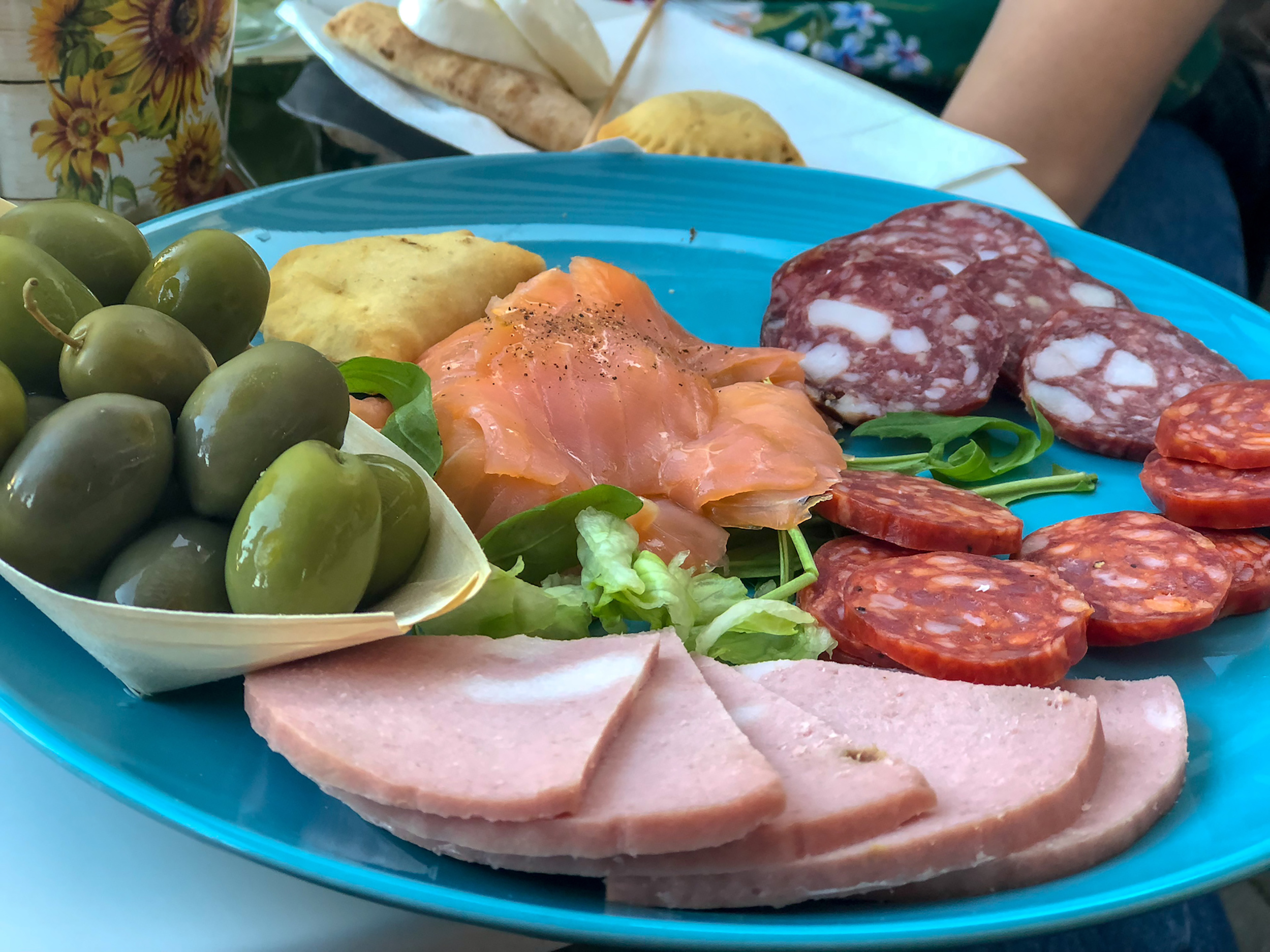 A plate of raw salmon, olives, bologna, and salami on a blue plate.