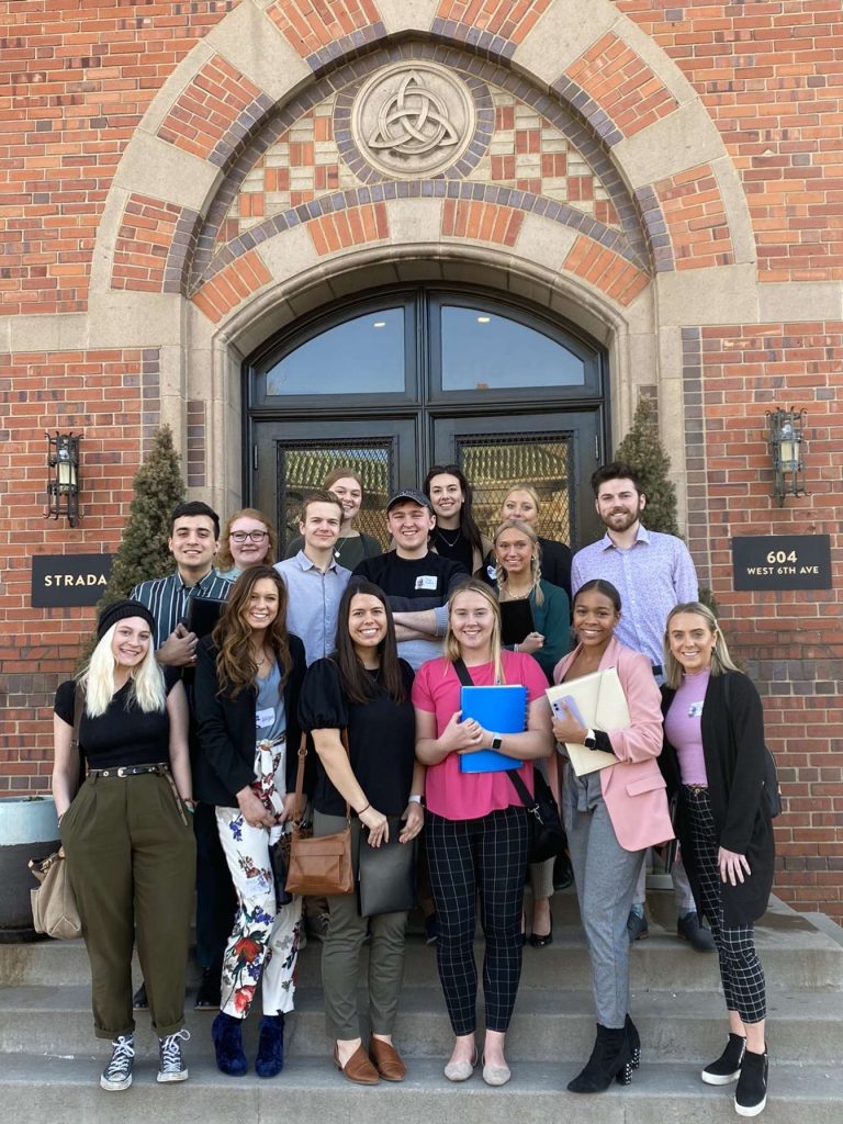 12 students on the steps outside a brick building