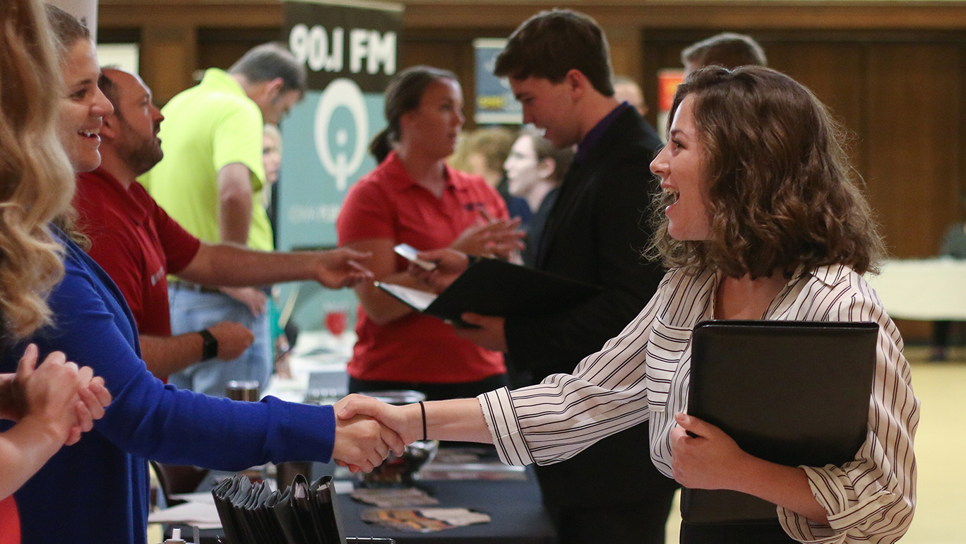 Female student shakes hands with employers at career fair