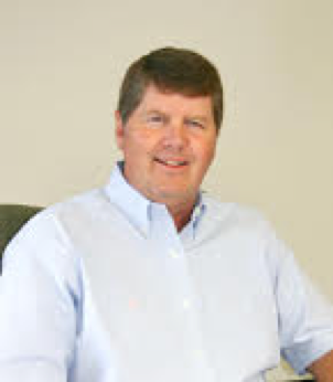 Jim smiles for the camera. He is wearing a blue shirt and has brown hair.