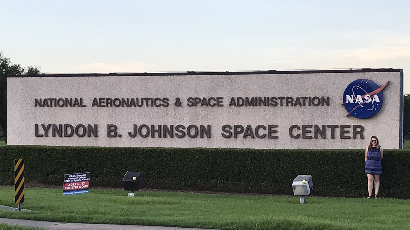 a female student stands in front of the NASA sign at Lyndon B. Johnson Space Center