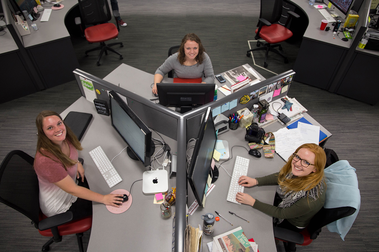 Three female students sit at their pod of three desks at the Iowa State Daily office.