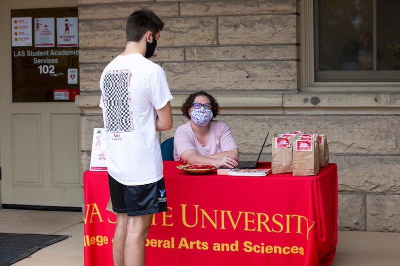 Woman at table talking to student standing in front of table.