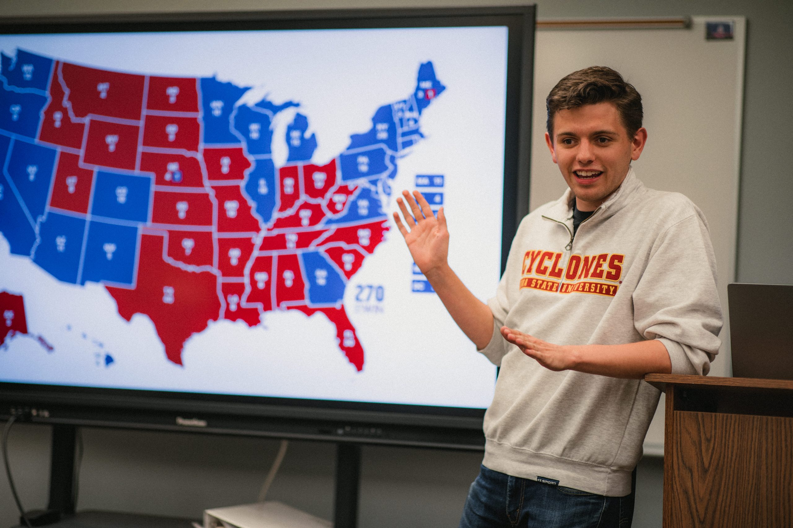 Student in an ISU quarter-zip sweater standing in front of a blue and red map of the United States of America