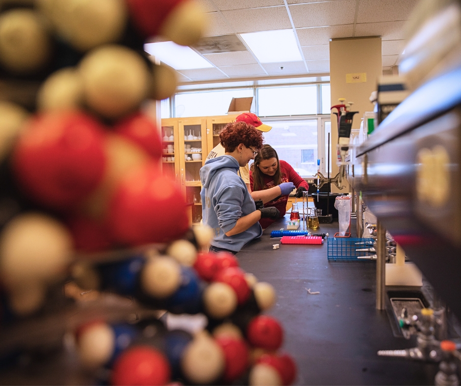 Two students working in a lab with molecule 3D model out of focus in the foreground