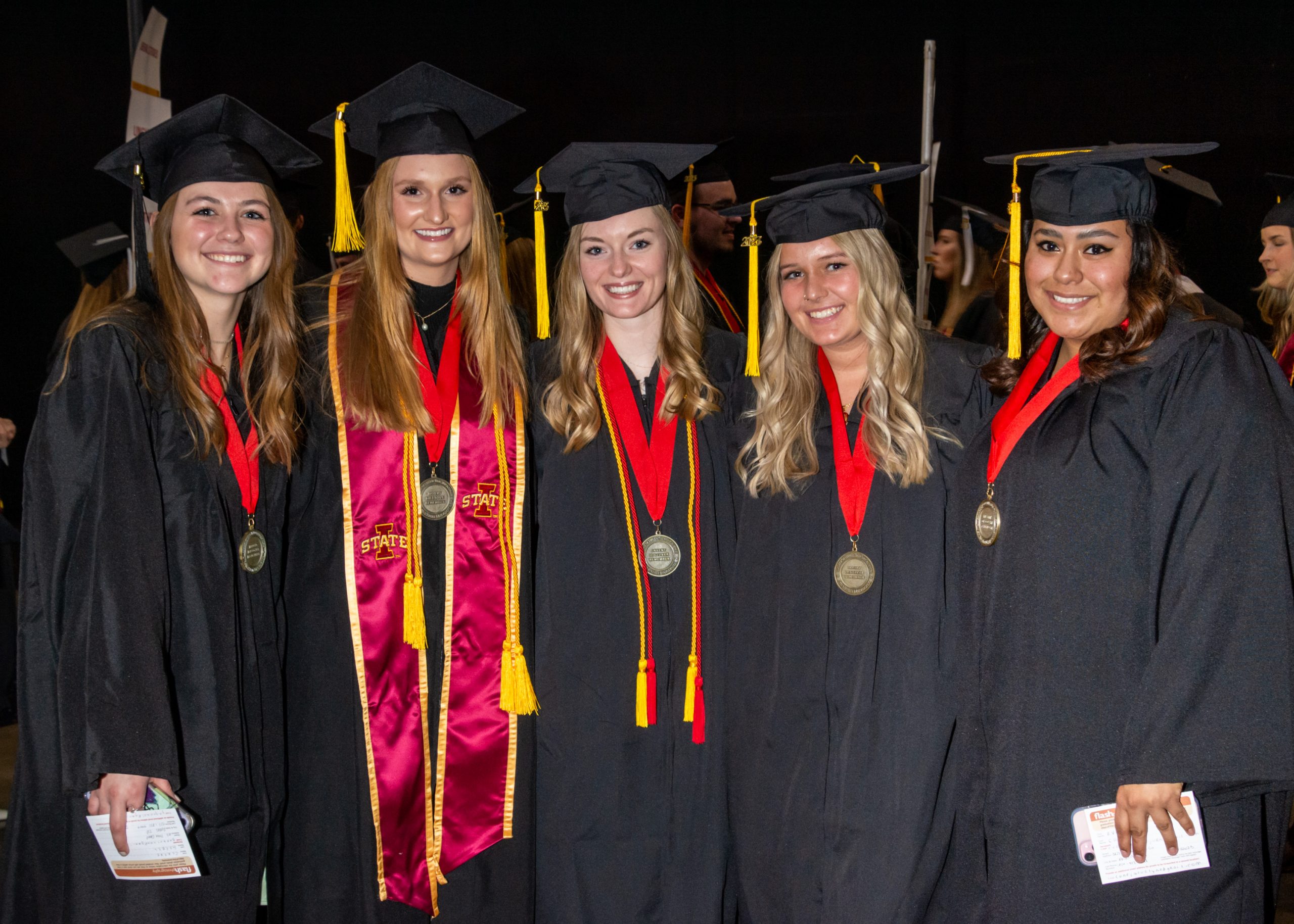 Five students wearing academic regalia and LAS medallions pose standing shoulder to shoulder smiling ahead of the Fall 2023 LAS Convocation Ceremony.