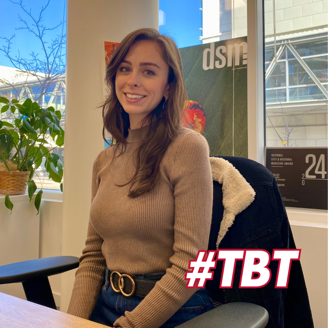 Hailey Evans ('20 journalism and mass communication) poses seated on a desk chair with a coat hanging from it. She is wearing a beige, long-sleeved sweater and is smiling directly at the camera. Behind her is a window which is partially covered by a dsm magazine cover.