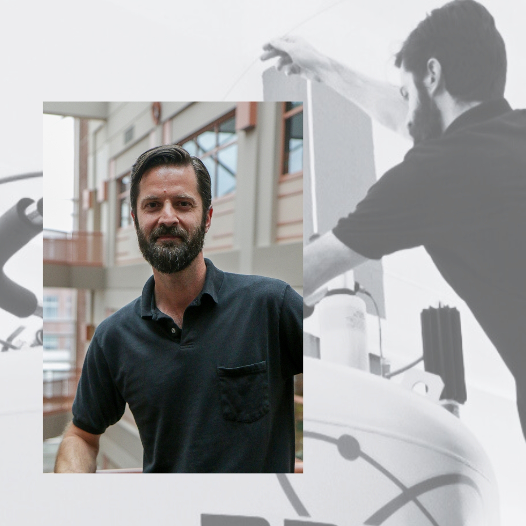 Julien Roche, wearing a black polo shirt, stands in a modern atrium with large windows. A faded, black-and-white overlay in the background shows him working with scientific equipment.