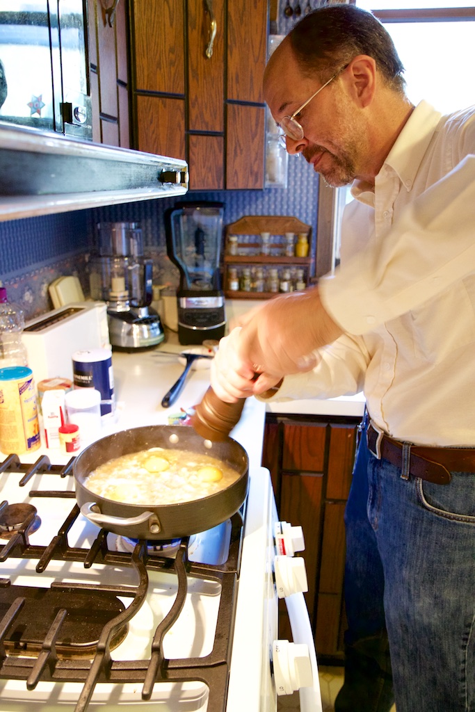 Paul Canfield stands at the stove putting salt into a dish in a large frying pan.