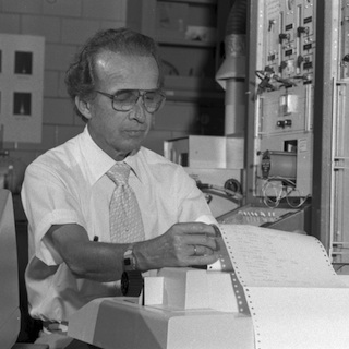 A black and white photo of Velmer Fassel reading a printout from an machine.