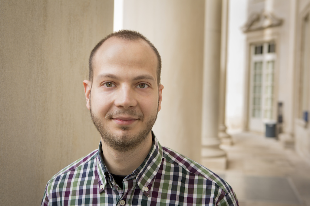 A portrait style close-up of Goran Micevic beside a building with stone columns.