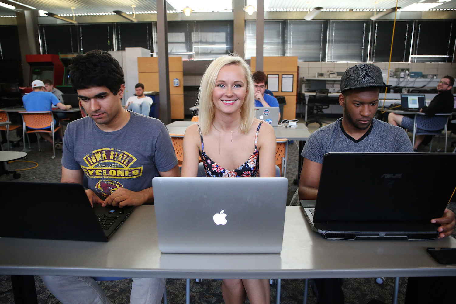 Kelsey Hrubes sits at her mac laptop between two men on their laptops.