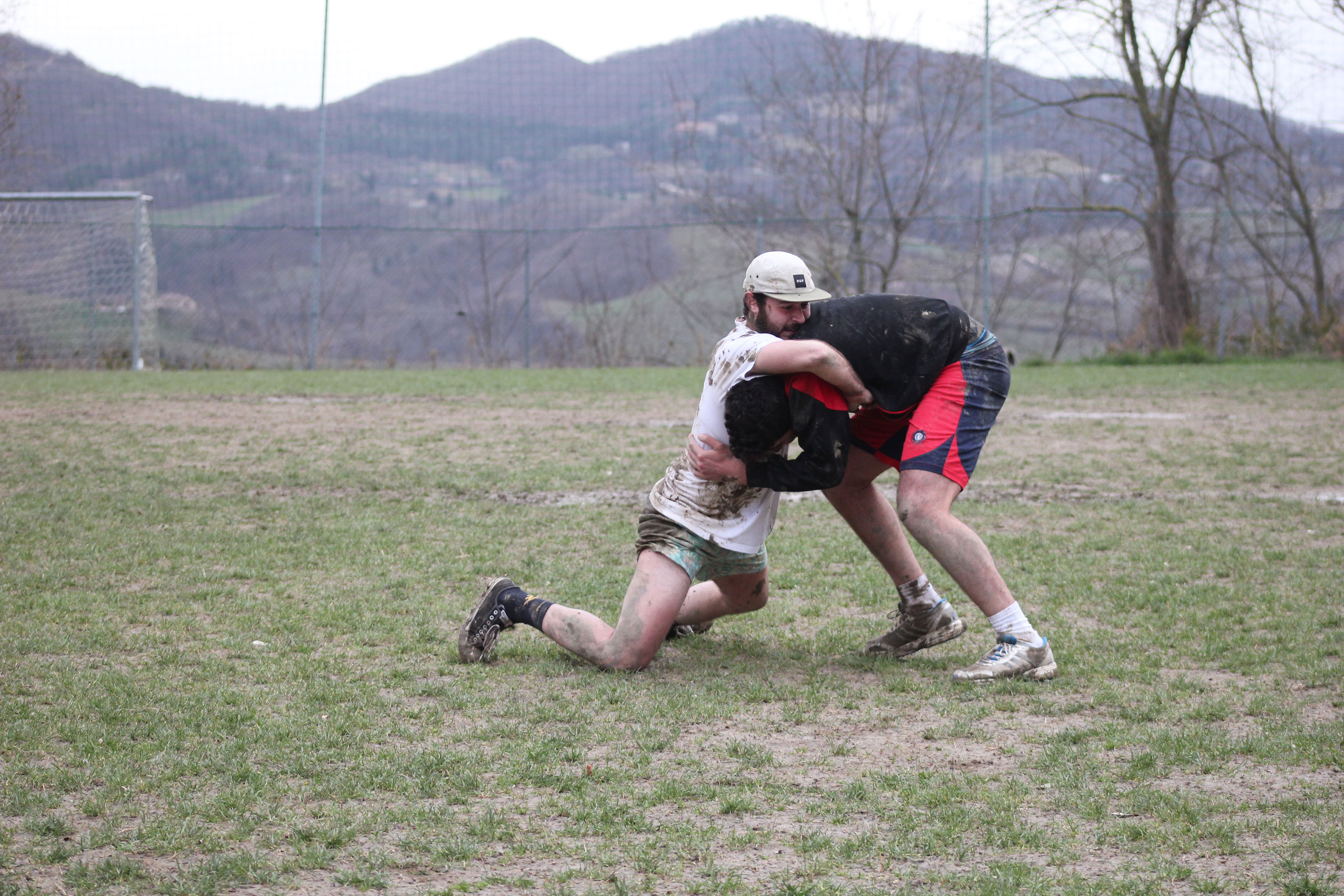 Two men wrestle on a field with hills in the background.