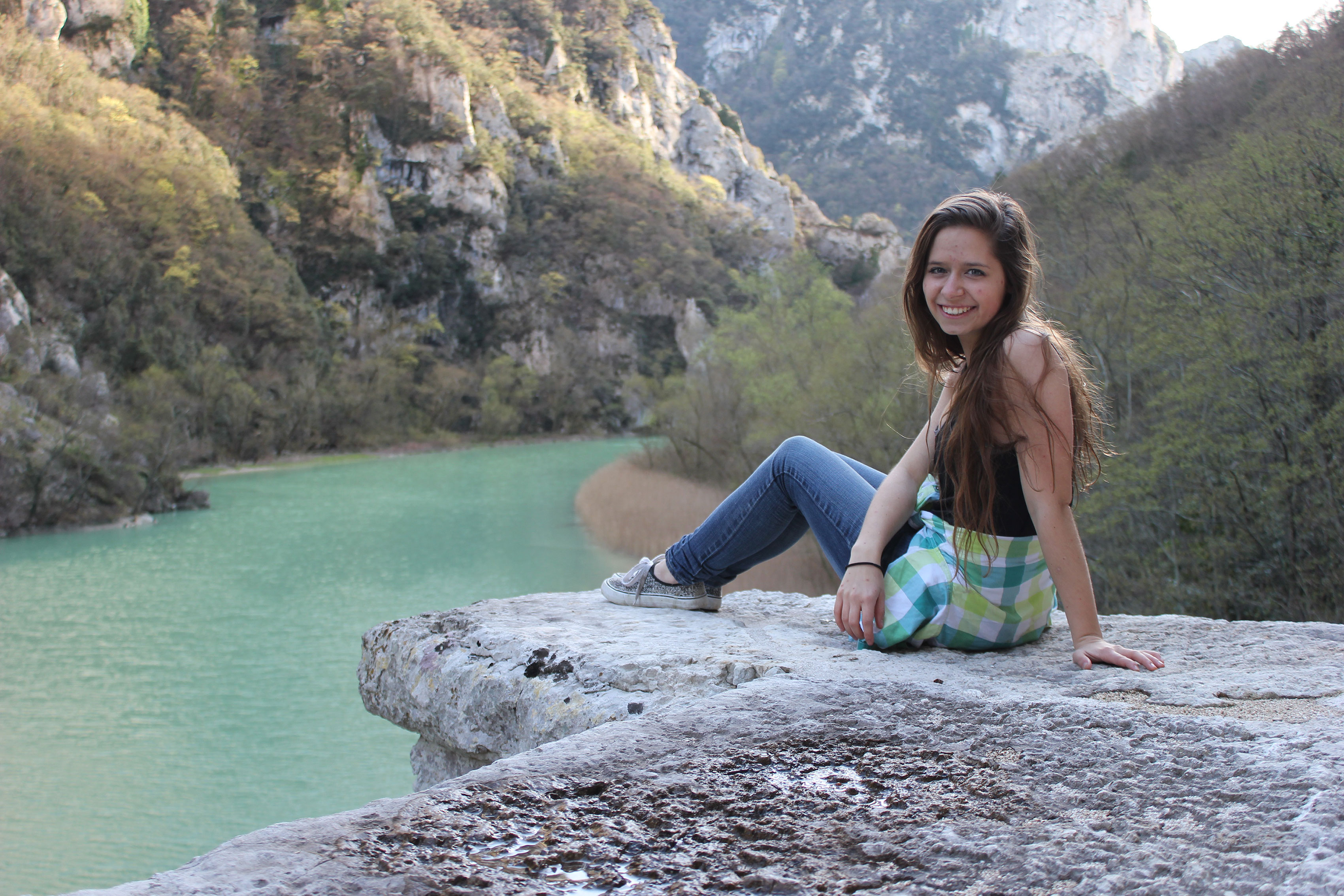 Jeni Zernick sits beside a gorge with an aqua blue river and hills rising on either side.