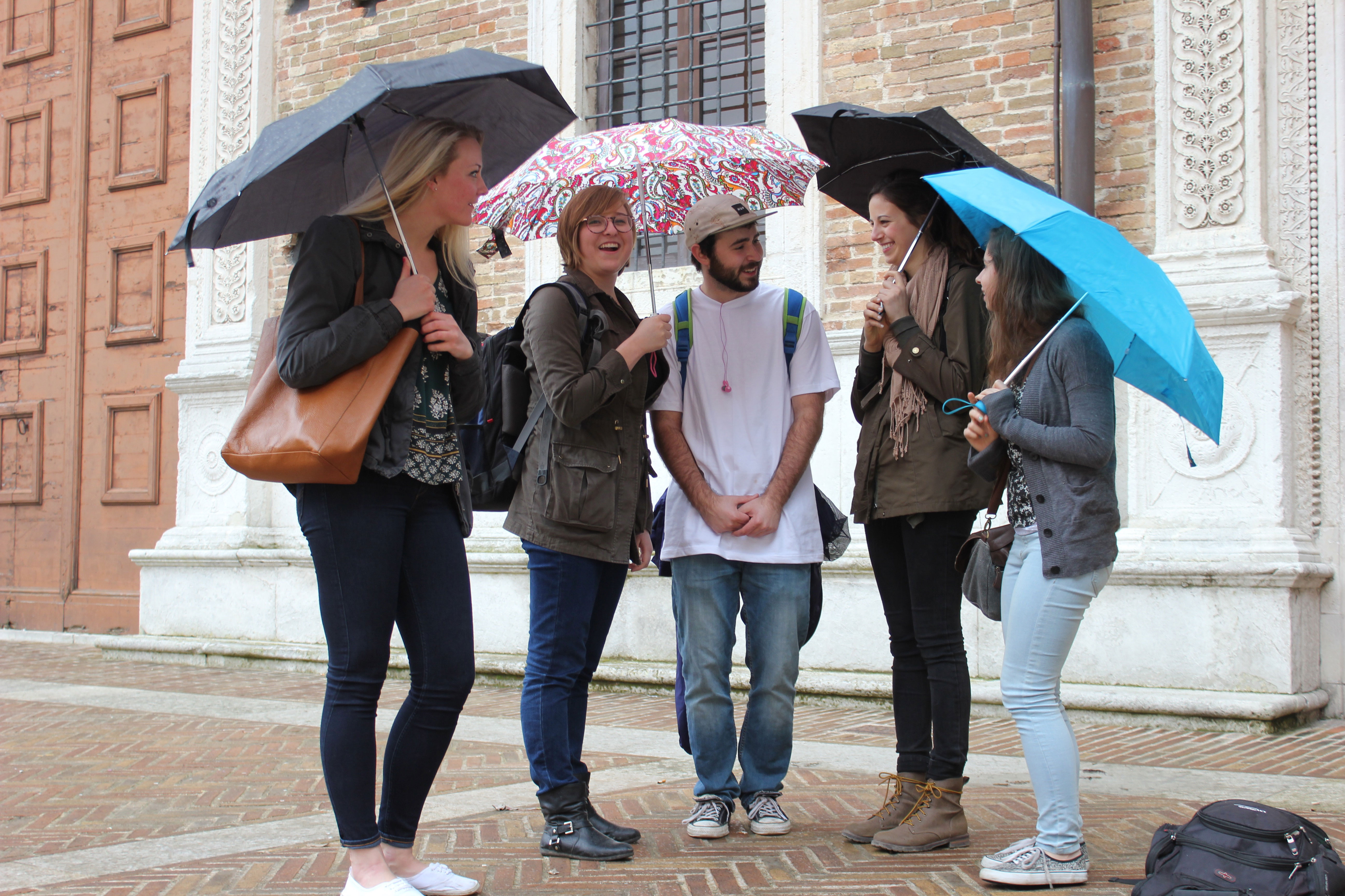 Students stand together under umbrellas outside a building.