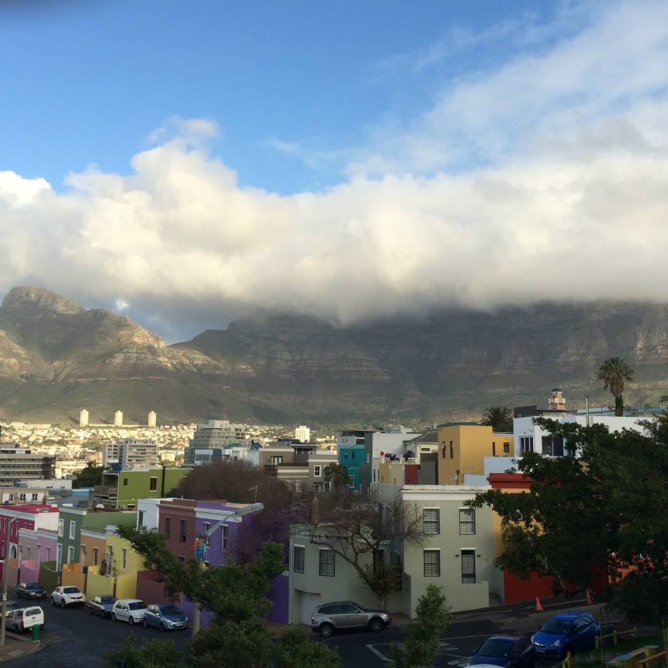 Landscape photo of Cape Town, South Africa, with a street of colorful houses in the foreground and mountains in the background.