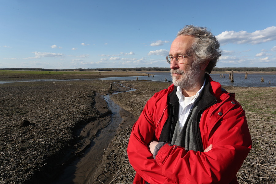 Bill Gutowski stands outside in a red coat by a wetlands area.