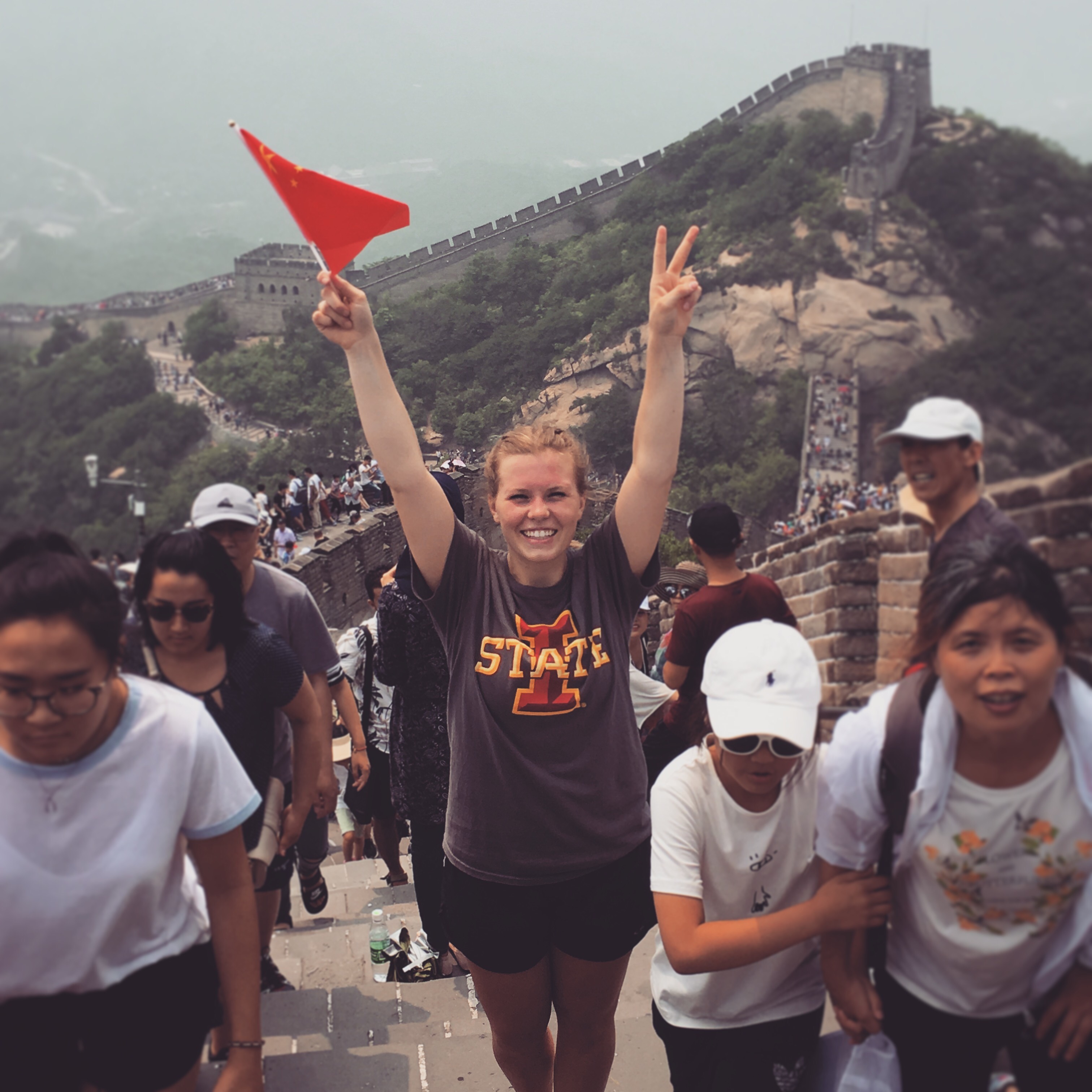 Student wearing ISU t-shirt stands with arms in the air on the Great Wall of China.