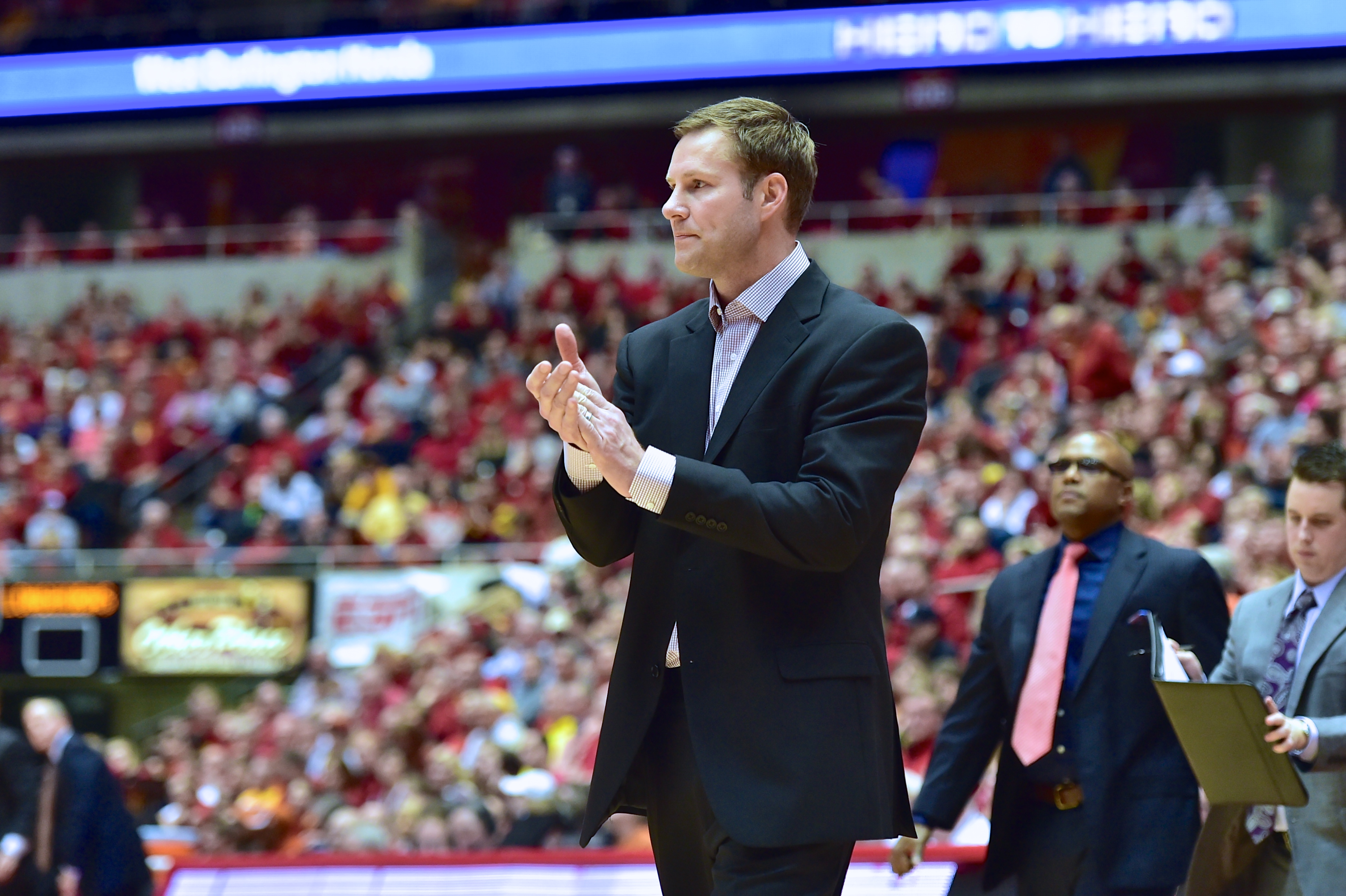 Hoiberg stands on the sidelines of Hilton Coliseum. Assistant coaches and Iowa State fans are in the background.