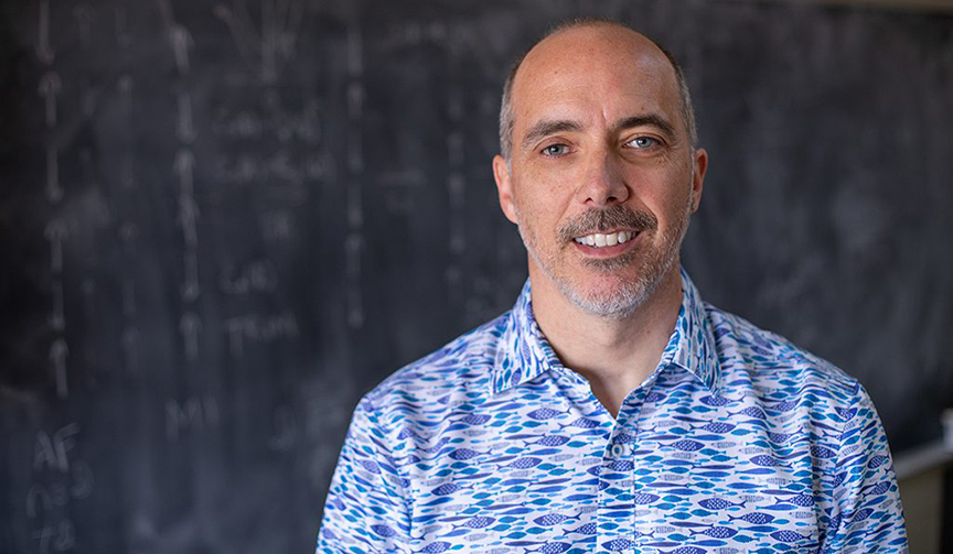 Robert McQueeney stands in front of a blackboard in his office.