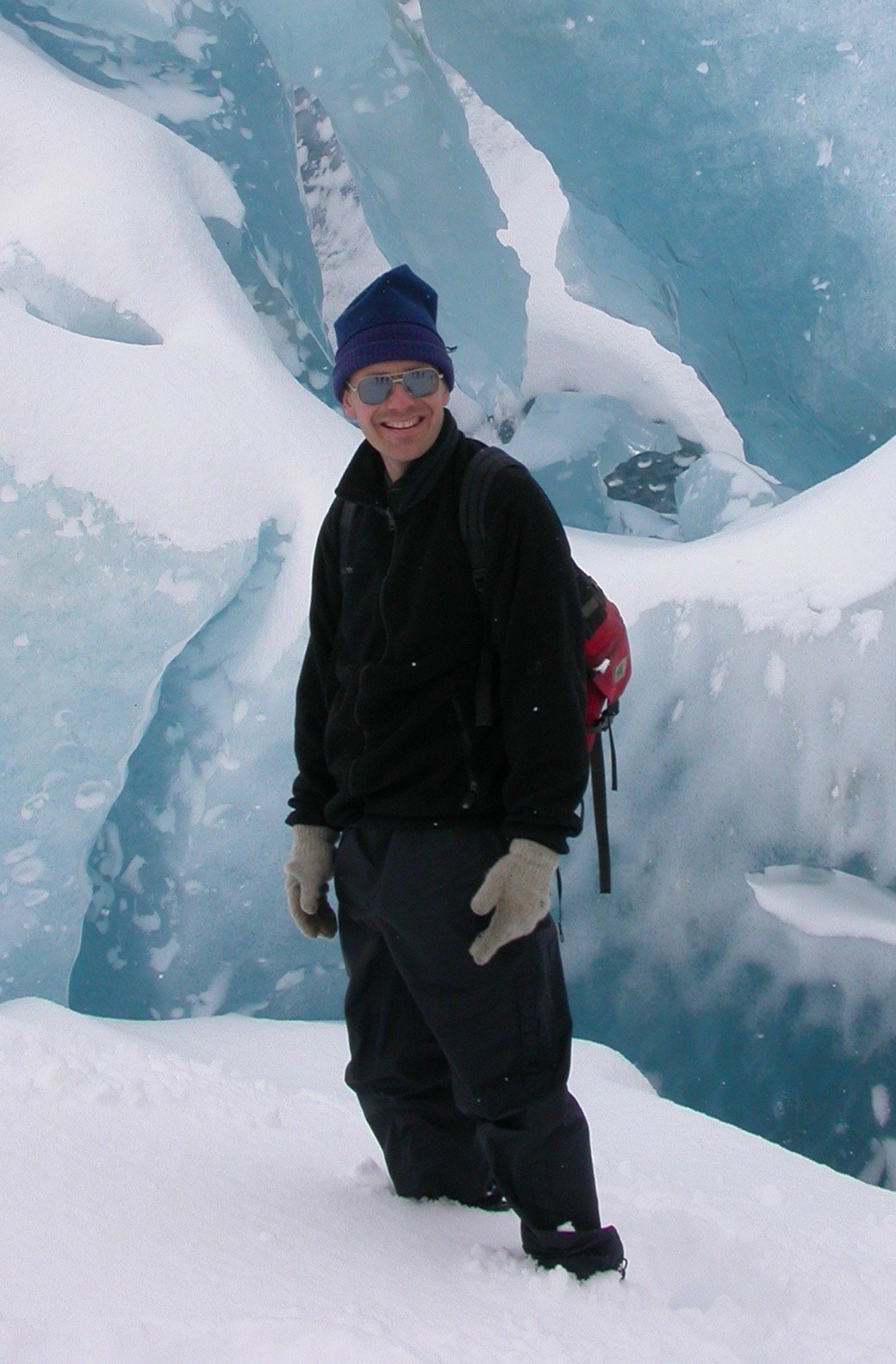 Neal Iverson, bundled in winter gear, stands in snow in front of a wall of ice.