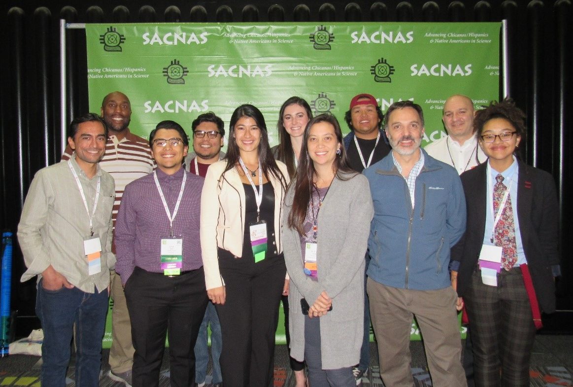 Students and faculty stand in front of a banner wearing their conference badges.