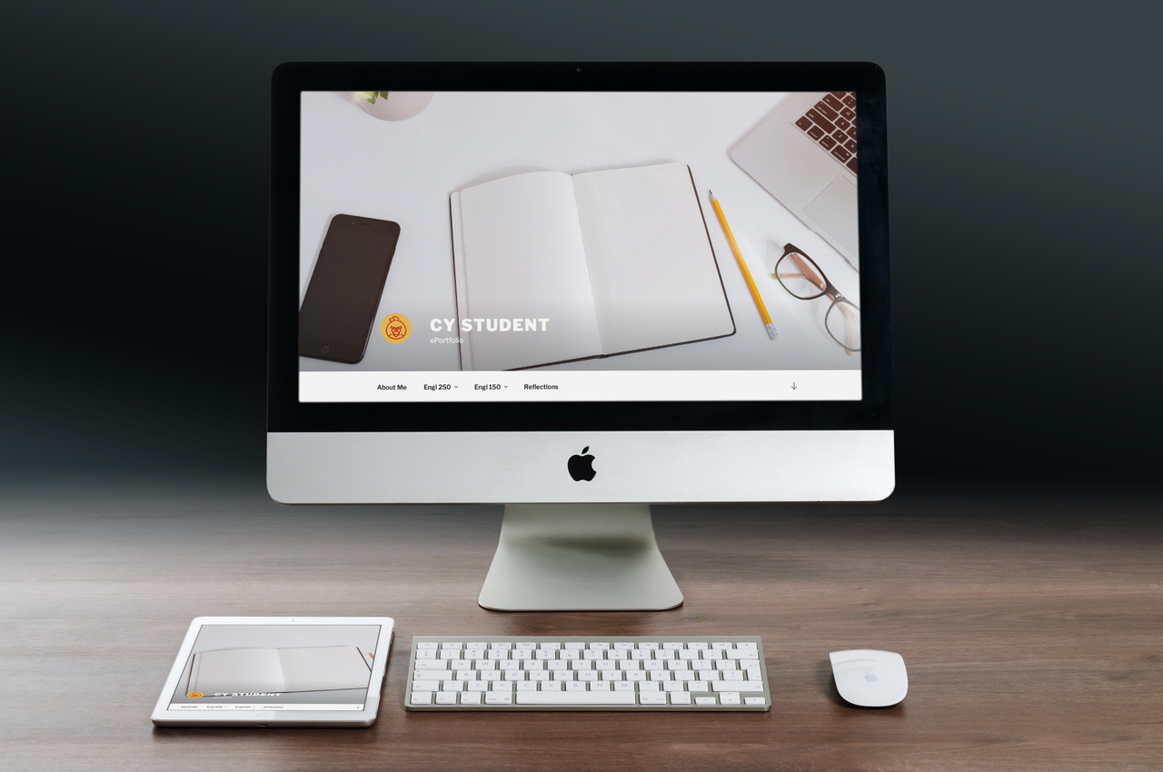 An apple computer on a desk with an ipad, keyboard and mouse beside it. The computer shows an ePortfolio on the screen.