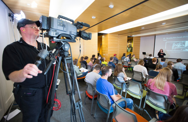 A cameraman records a lecture in a classroom.