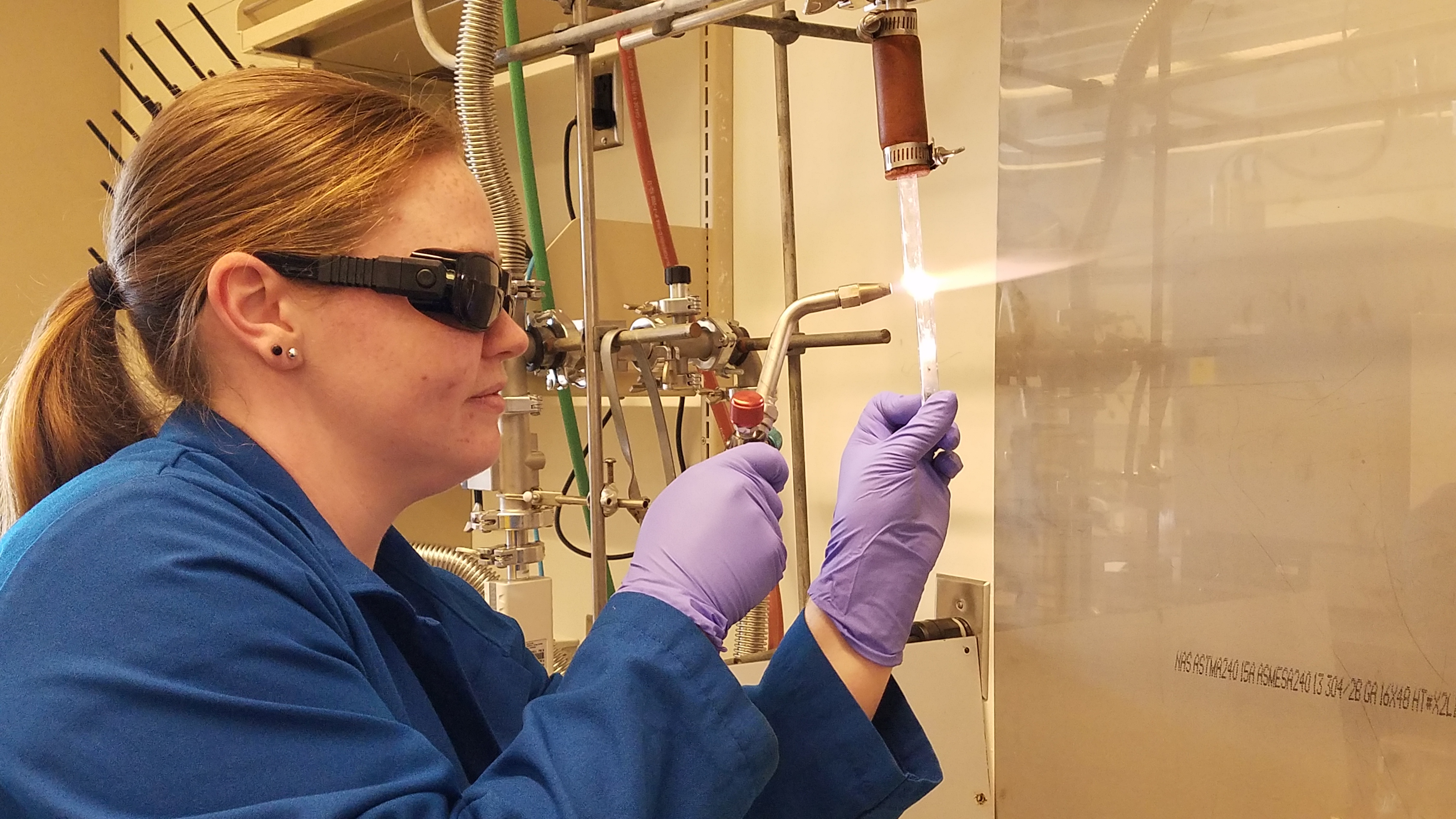 Shannon Lee holds a small torch up to a glass tube.