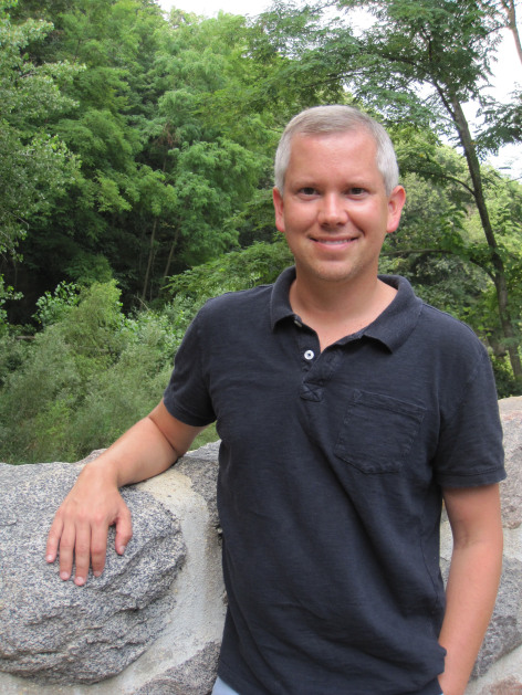 Matthew Hufford outside beside a rock in front of trees.