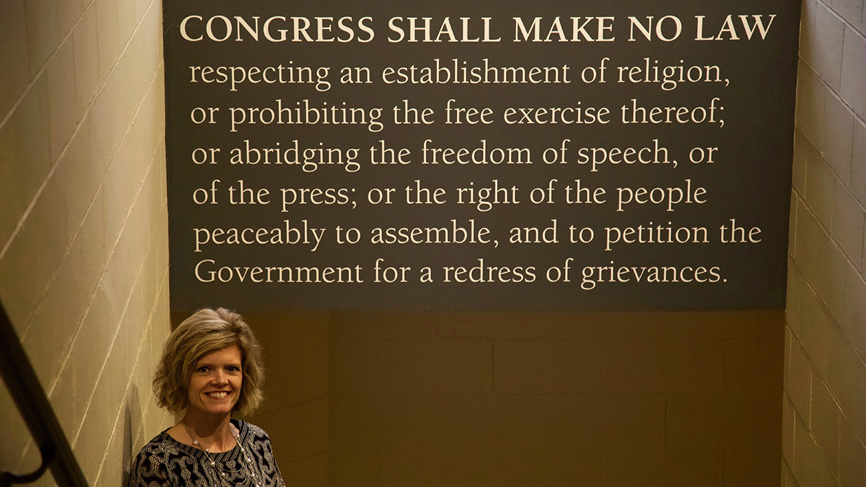 A woman stands in front of a sign with the first amendment written on it.