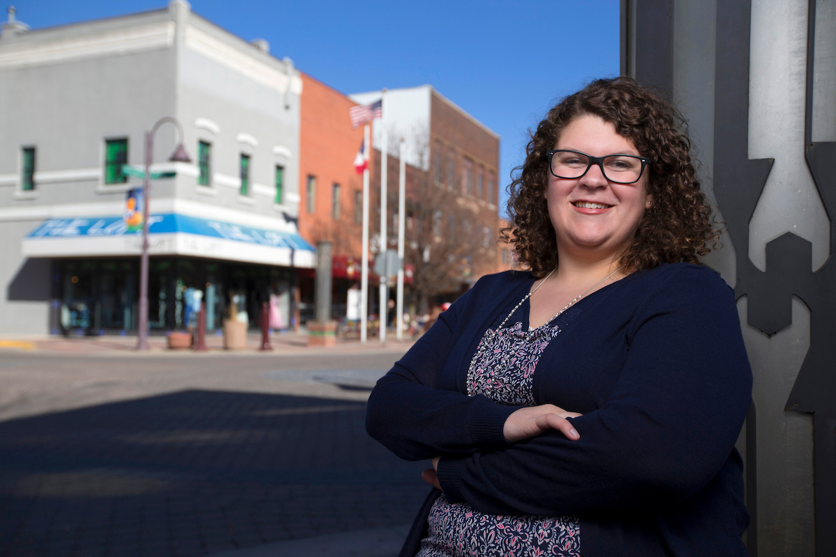 Danielle Propst stands in a community showing a street with shops.