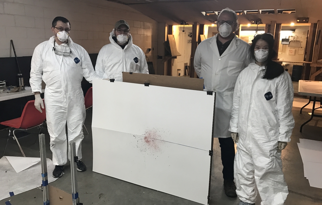 People in hazmat gear stand by a blood stain pattern