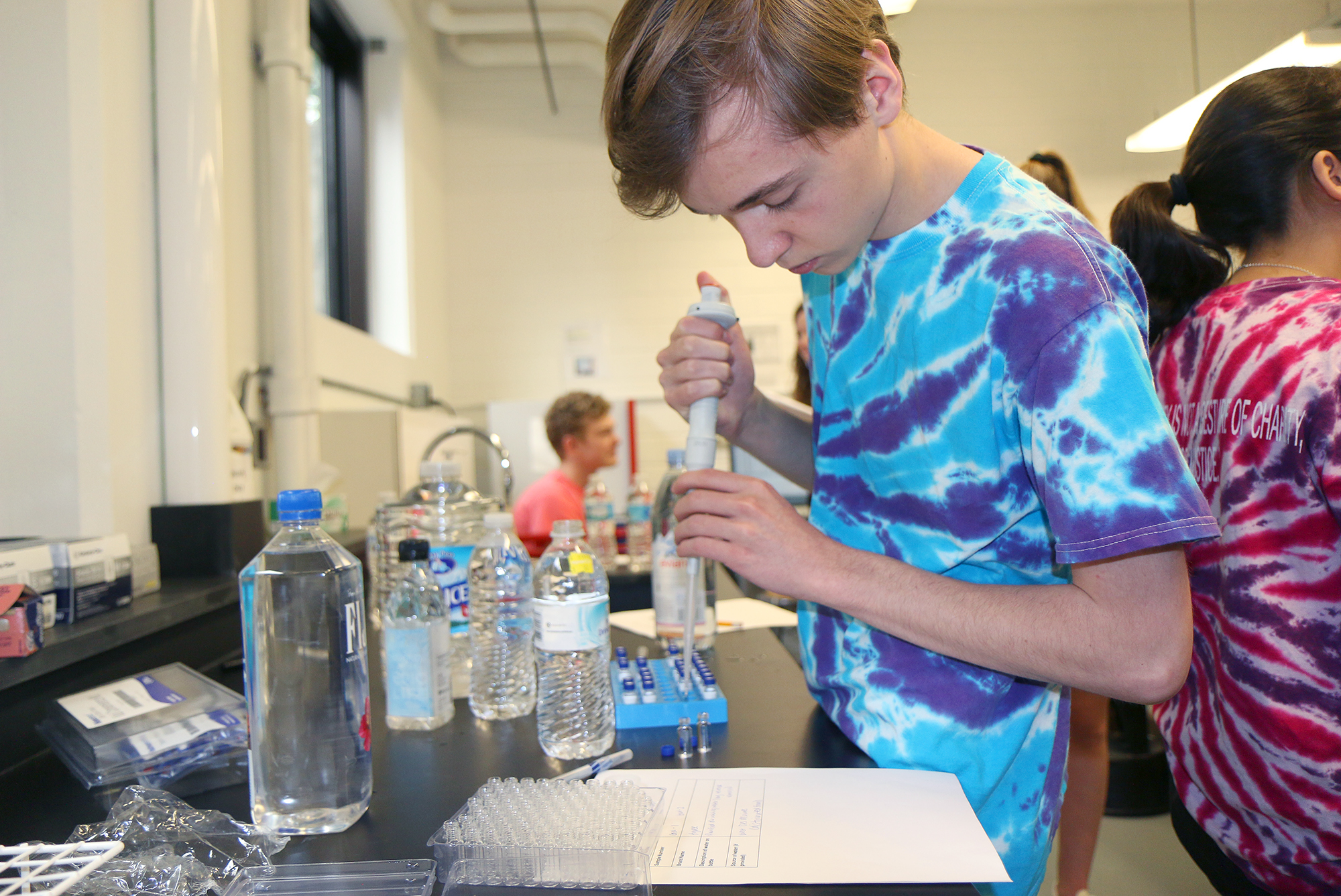 Brennan stands at a table with a large pipette and a water bottle.