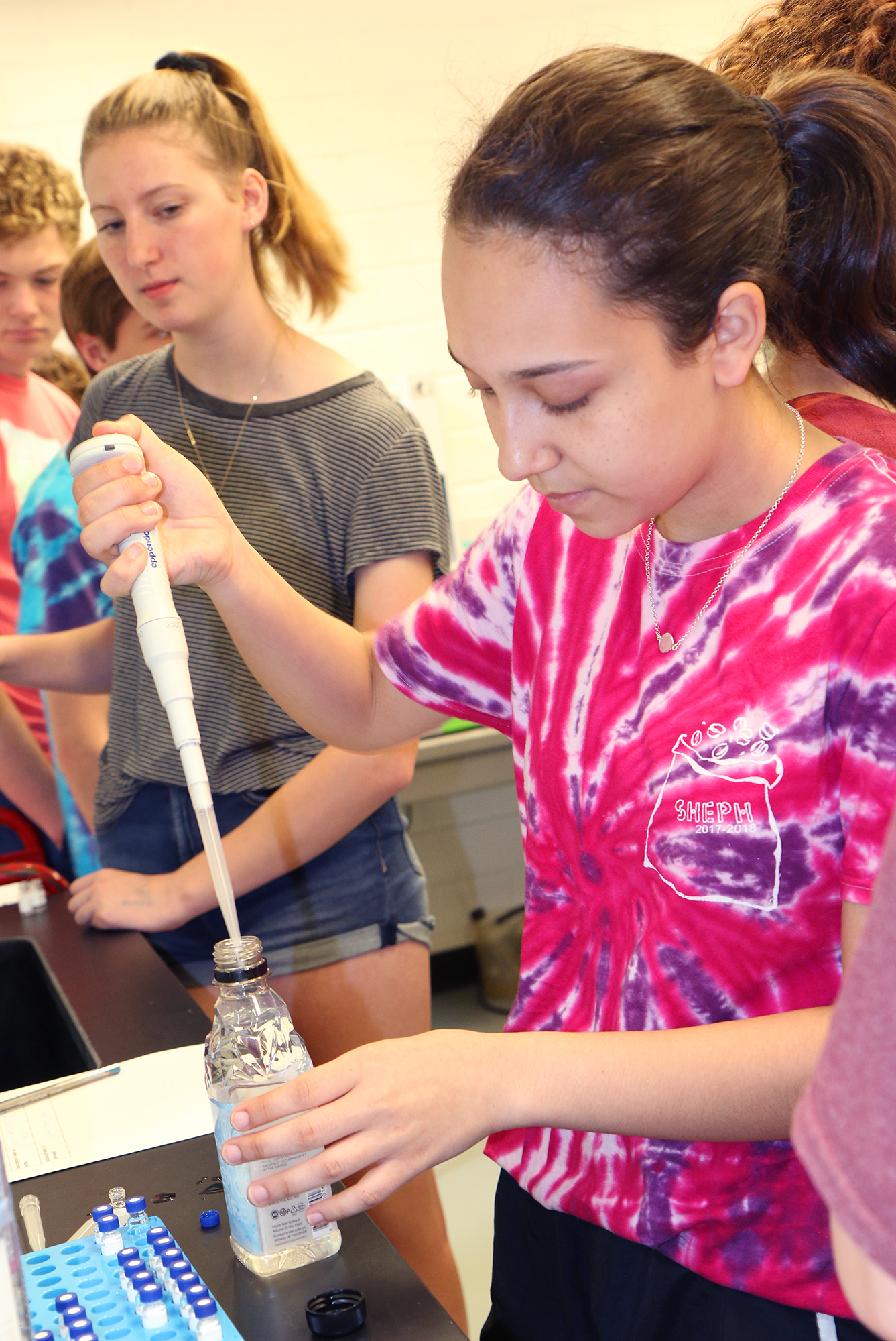 A girl stands at a counter using a large pipette.