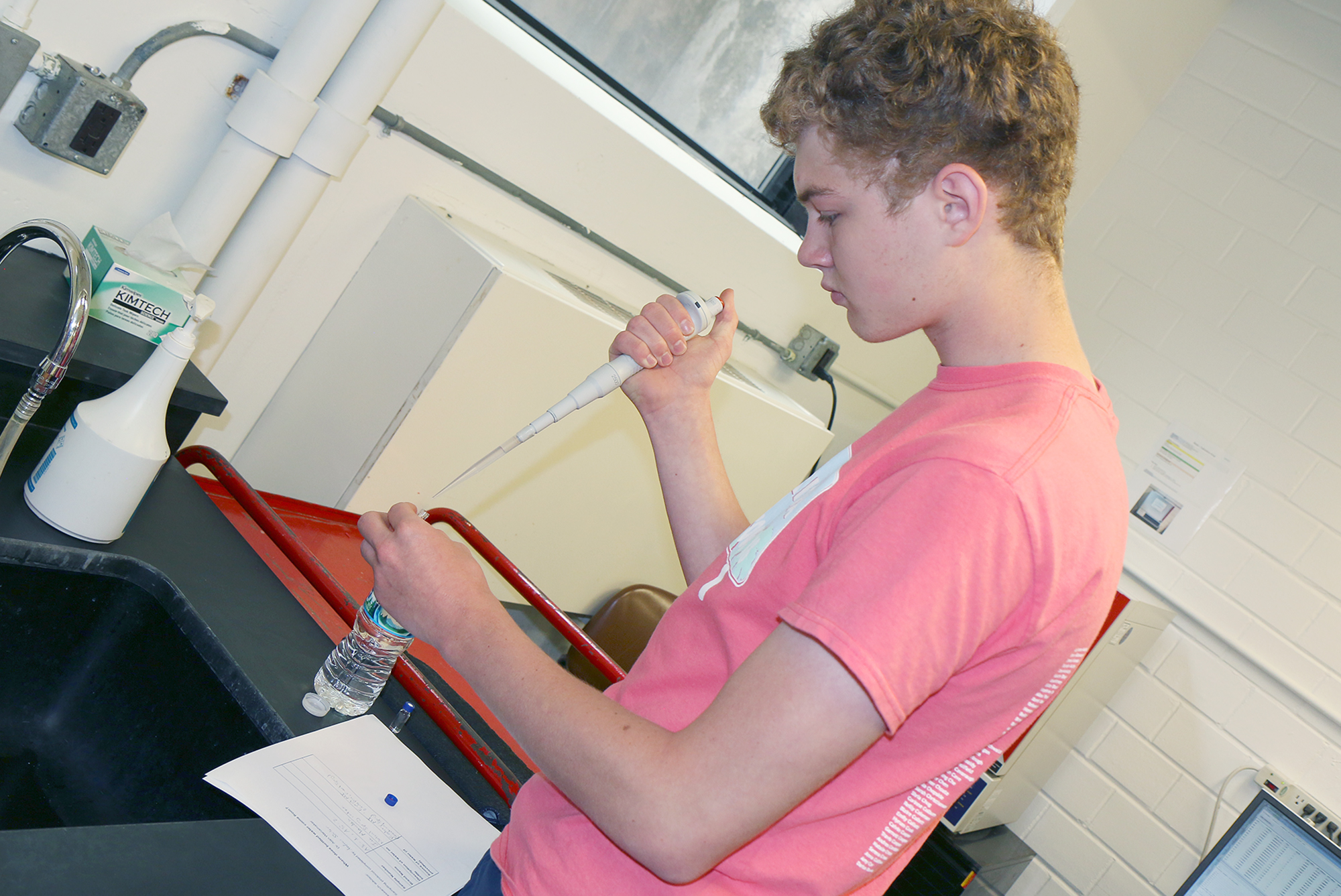 Student stands at a counter using a large pipette.