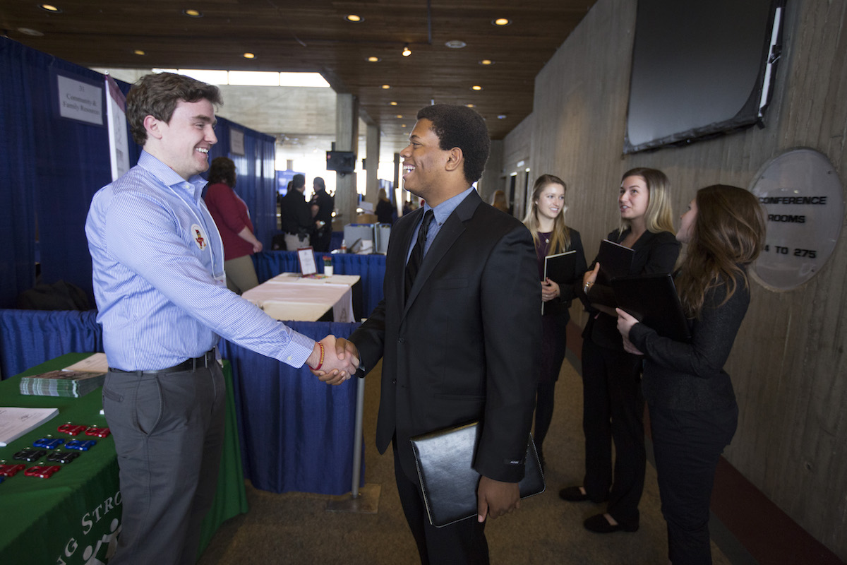 One student shakes hands with a company representative while other students wait.