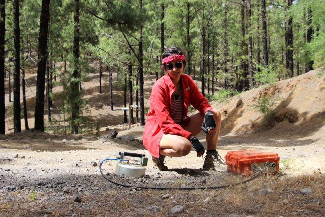 A student kneels in a forest with research equipment.