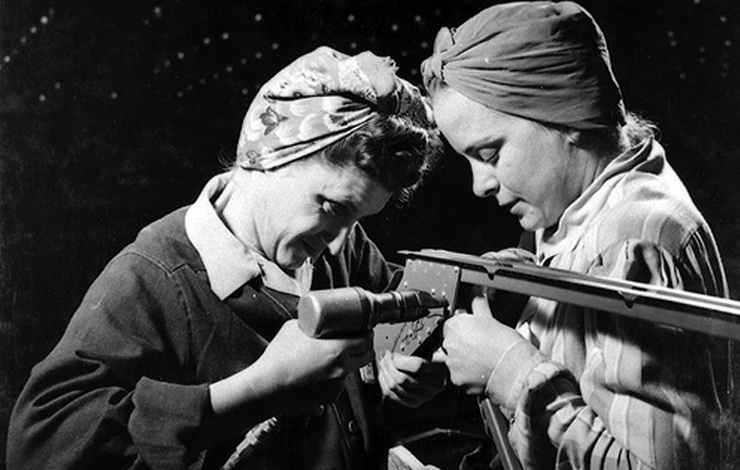 Two women work on a piece of machinery.