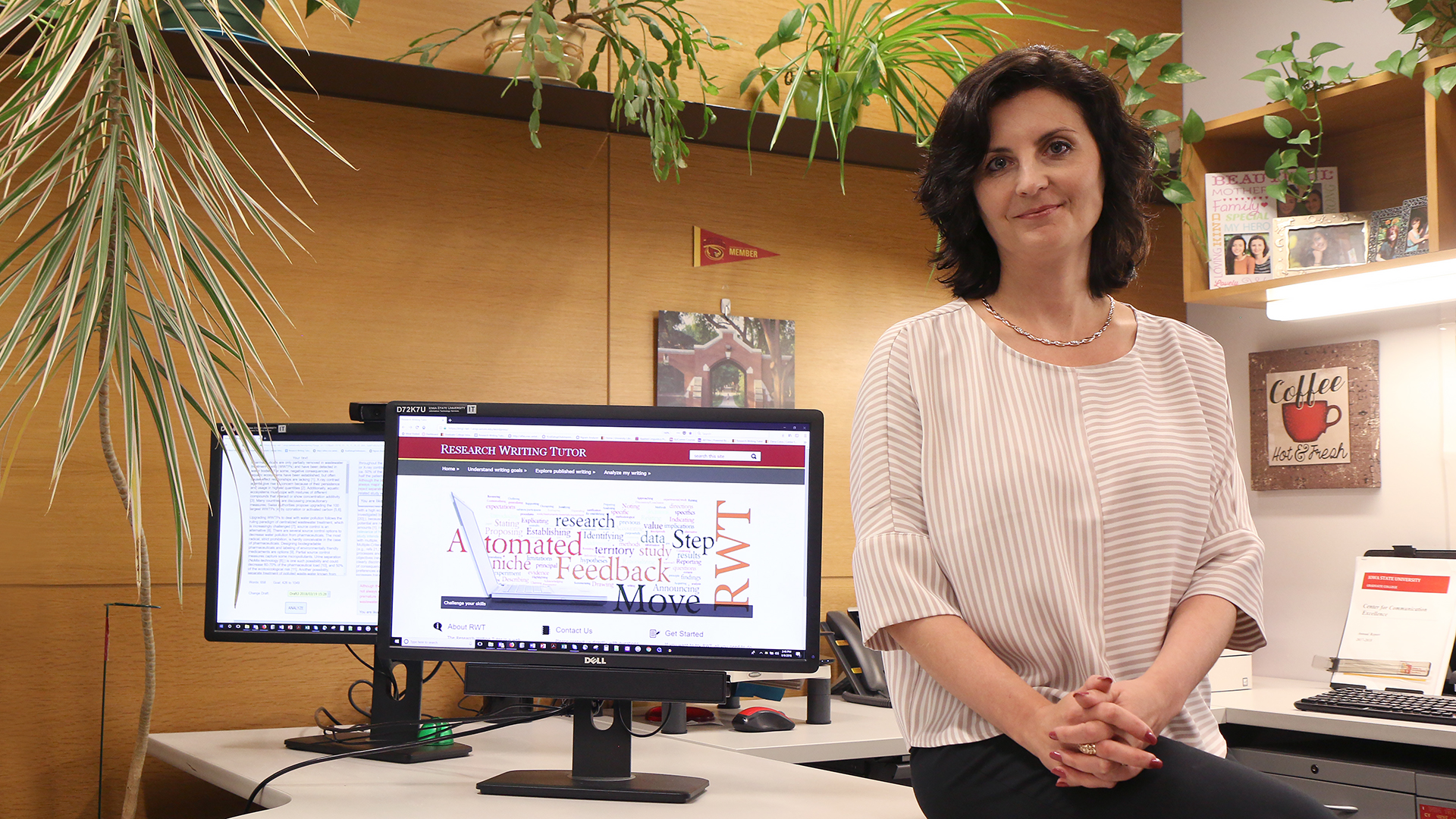 A woman in an office with computer monitors showing a writing evaluation tool.