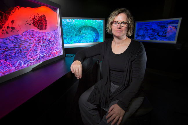 Photo of woman in front of three colorful etched glass panels.