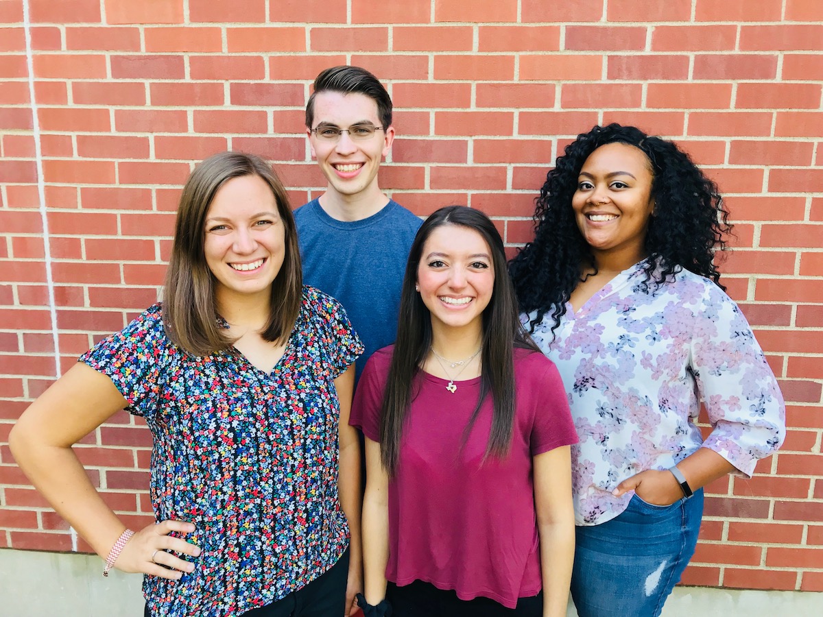 Four college students standing and smiling at the camera