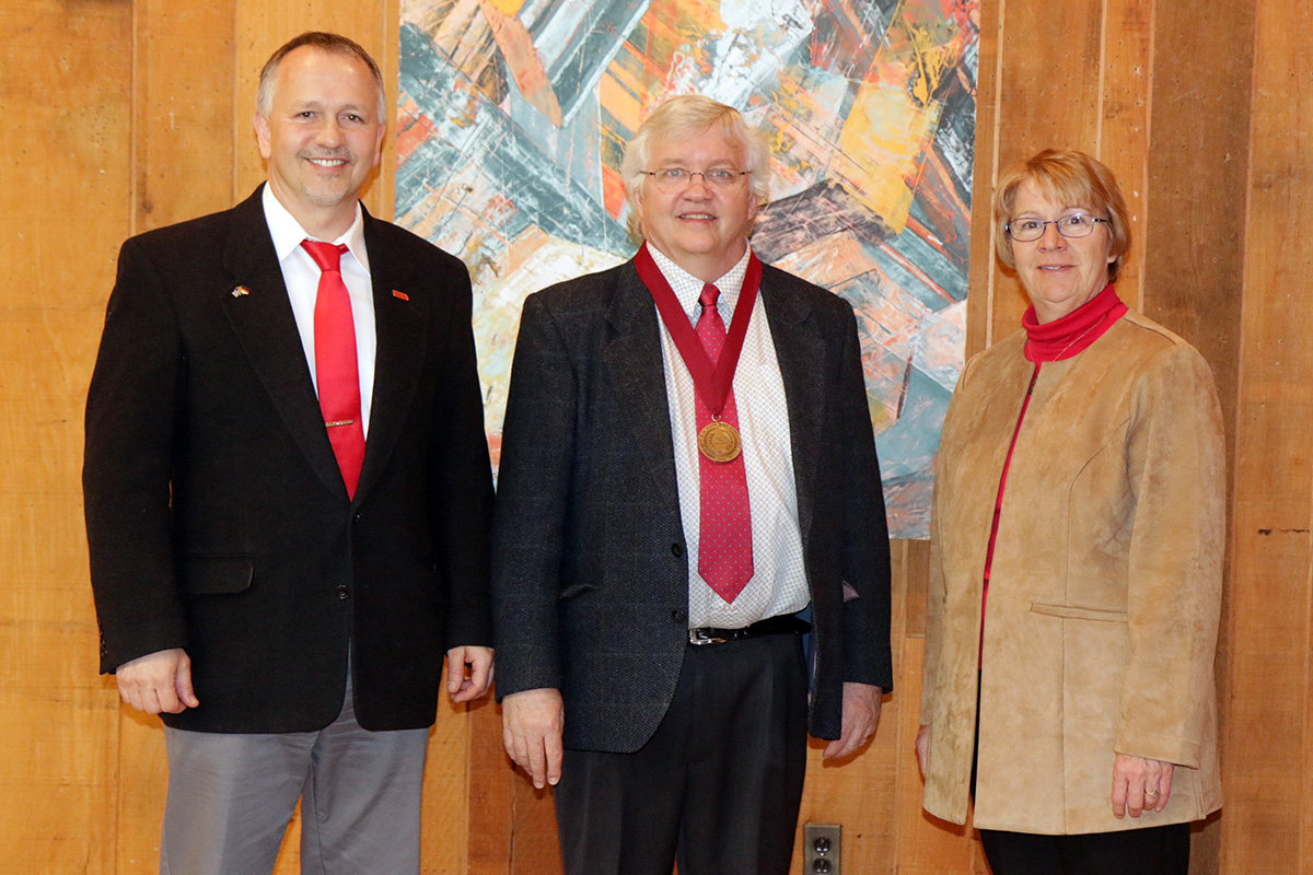 Three people, with medal recipient in the middle