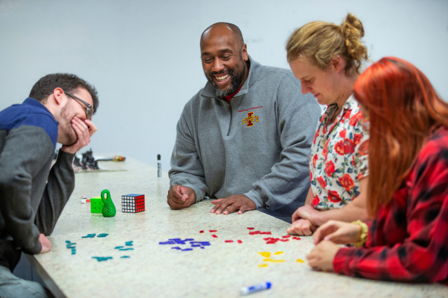 Michael Young sits at table with three other people, laughing and demonstrating math in a fun way