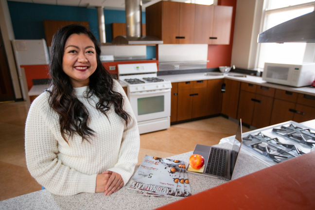 Woman standing at counter in kitchen, with a magazine on the counter.