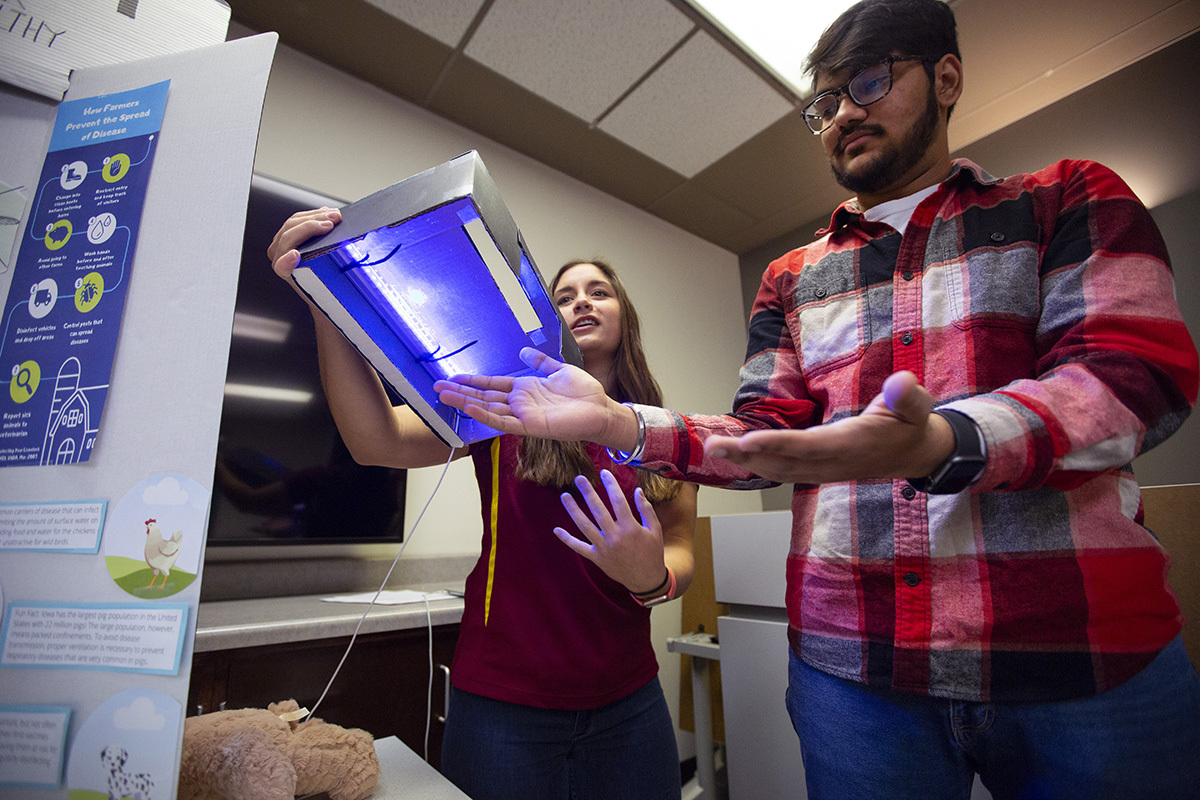 Two students using a boxed ultraviolet light to examine hands for contamination.