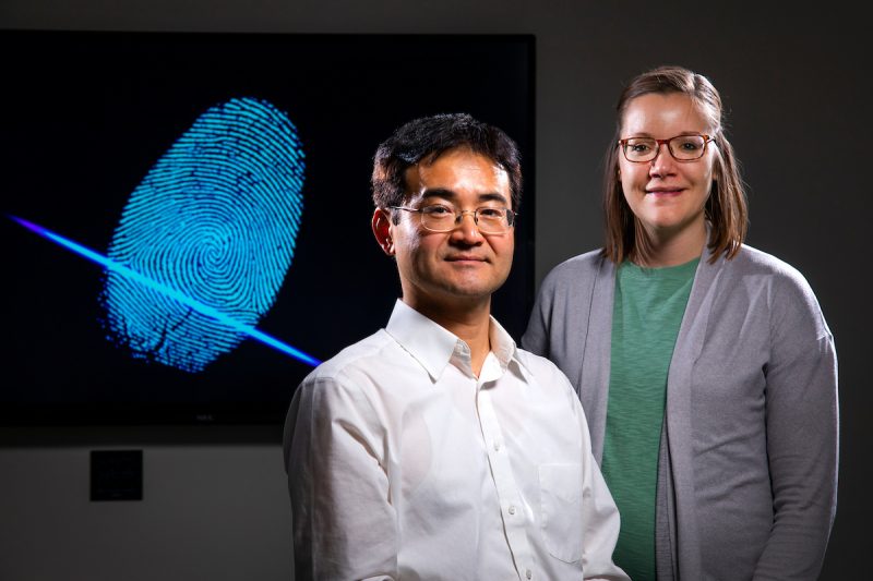 Chemists Young-Jin Lee and Paige Hinners sit in front of a project image of a fingerprint